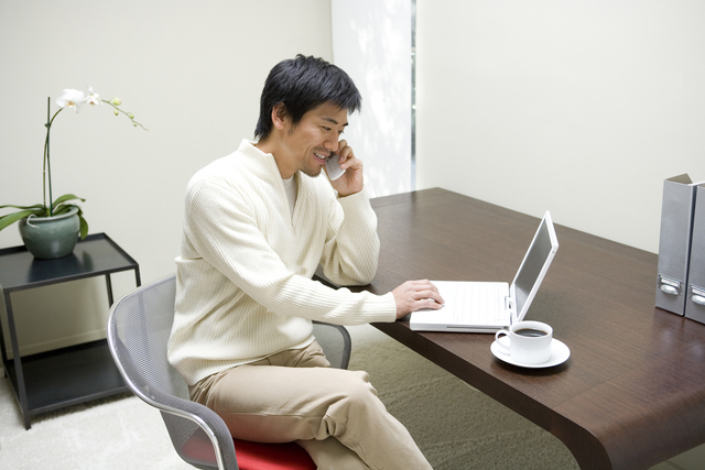 男性がパソコンの前で携帯で会話している